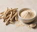 Bowl of ashwagandha root powder beside dried ashwagandha roots on linen